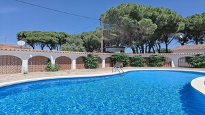 Una piscina con bordo piastrellato, circondata da un muro bianco con aperture ad arco e una recinzione in legno.