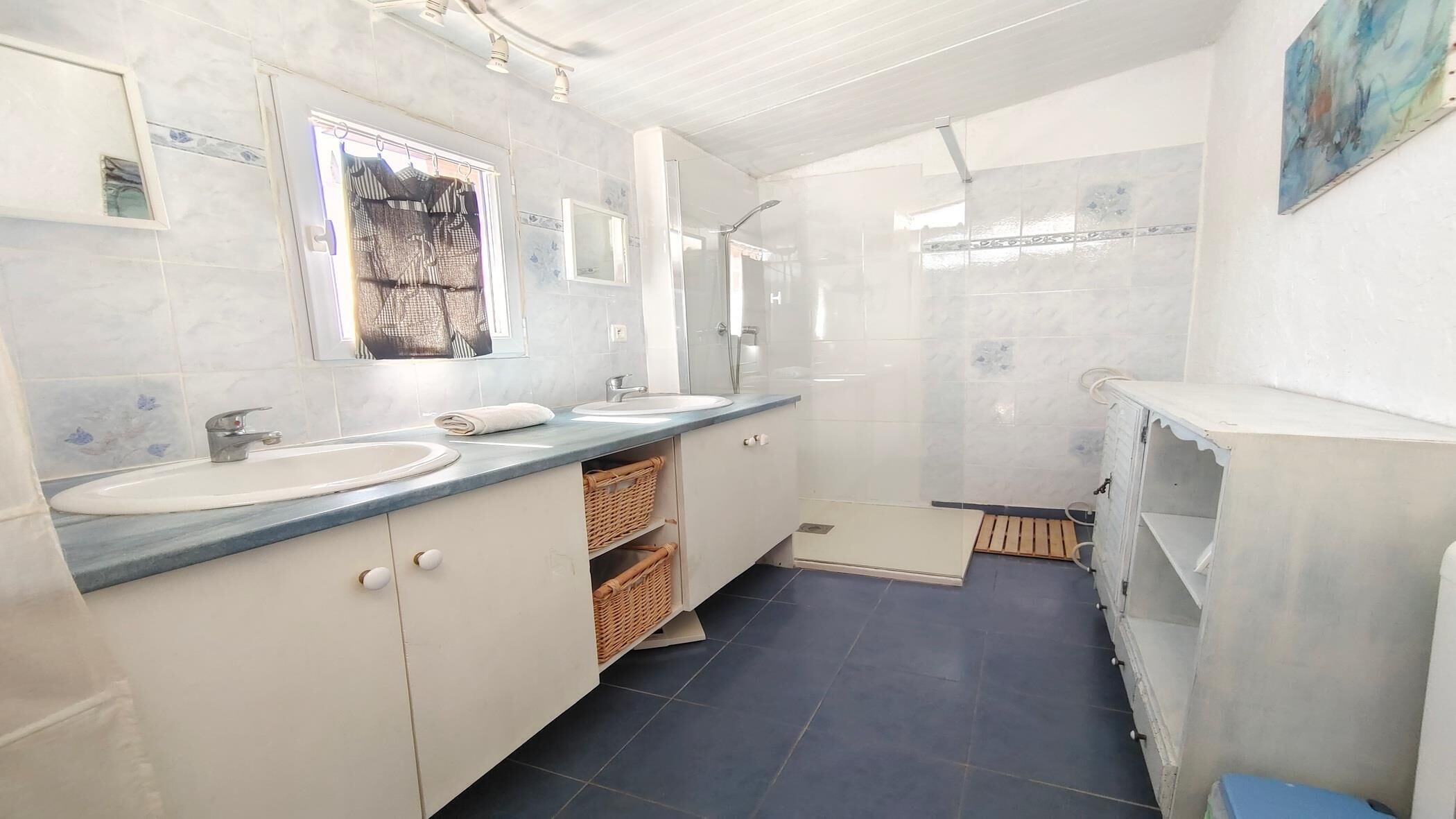Une salle de bain avec deux lavabos, une douche et un meuble avec des paniers.