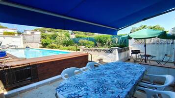 Un espace aménagé au bord de la piscine, comprenant un coin salon couvert, un jacuzzi et un barbecue.