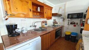 Une cuisine compacte avec des meubles en bois, un four à micro-ondes encastré, une cuisinière à gaz, un évier et un lave-vaisselle.