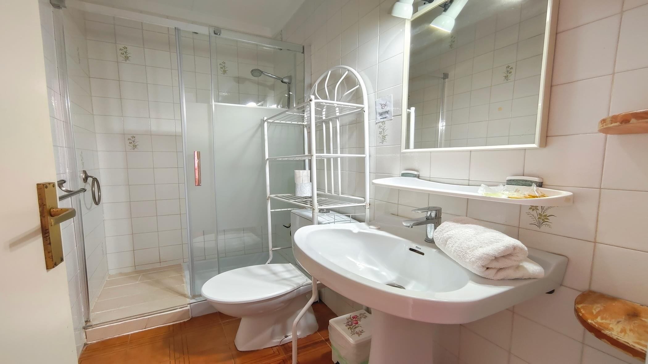 Un bany amb un box de dutxa de vidre, un vàter, un lavabo amb una tovallola i un mirall.