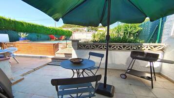 Une terrasse avec une table, des chaises, un barbecue et une piscine en arrière-plan.