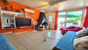 Un salon équipé d’un téléviseur, de la climatisation, d’un ventilateur, d’un barbecue et offrant une vue sur l’extérieur.