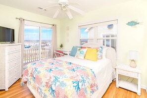 A bedroom with a bed, a television, a window with a view, and a ceiling fan.