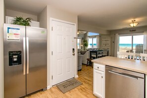A kitchen with stainless steel appliances, a white door, and a view of the beach through large windows.