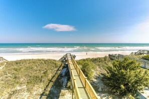 Een houten looppad dat naar een strand leidt, onder een heldere lucht.