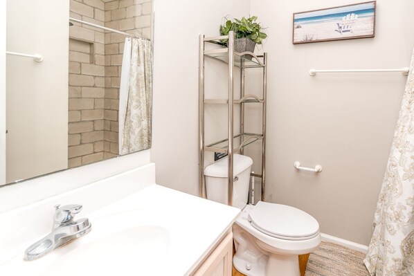 A bathroom with a white sink, a toilet, a glass shower enclosure, and a framed picture on the wall.