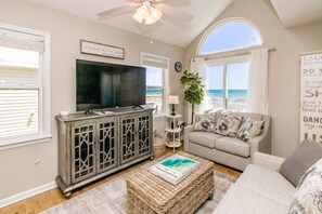 A living room with a television, a sofa, a coffee table, and a view of the beach. - Misty Morning North - 4BR Oceanfront Home; Dog Friendly! (North Topsail Beach)