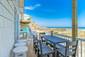 A wooden deck with a table and chairs, overlooking a beach with a wooden boardwalk and ocean view.