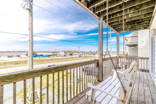 A wooden porch with a swing, overlooking a road with vehicles and industrial buildings.