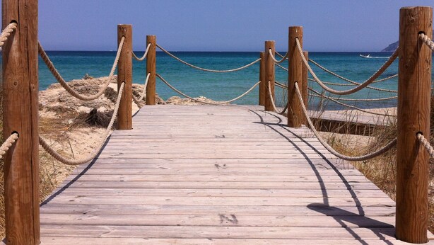 Une promenade en bois mène à une plage, avec un ciel bleu dégagé.