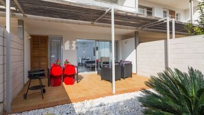 Un espace extérieur moderne, aménagé en patio, avec un coin salon abrité, un espace repas et un jardin agrémenté de galets blancs et de cactus.