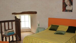 A bedroom with a bed, a small table with a lamp, a window, and a wooden chair with books. - Logis in the chateau enclosure (Paizay-Naudouin-Embourie)