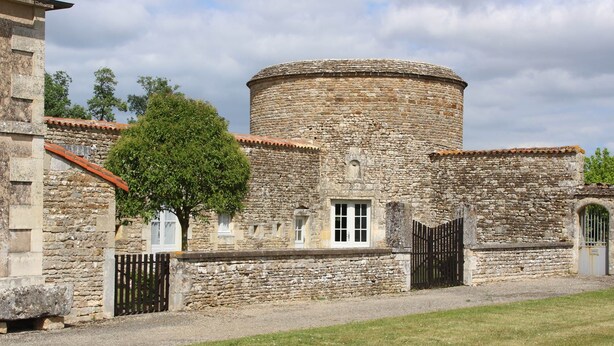 A stone building with a round tower, a gate, and a tree in front. - Logis in the chateau enclosure (Paizay-Naudouin-Embourie)