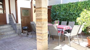A patio area with a stone pillar, outdoor seating, a grill, and a hedge wall. - Ferienhaus Landeskrone (Dresden)