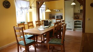 A dining area with a wooden table and chairs, a clock on the wall, and a kitchen in the background. - Ferienhaus Landeskrone (Dresden)