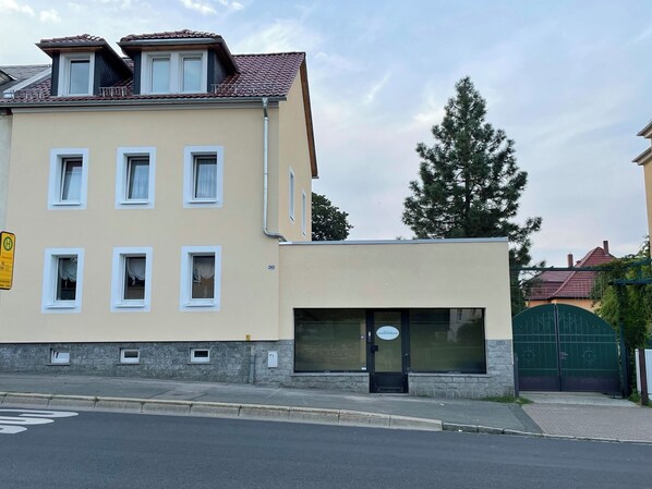 Ein Gebäude mit mehreren Fenstern, einer mit „LANDESKRENE“ beschrifteten Tür und einem grünen Tor im Hintergrund.