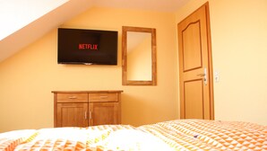 A room with a bed, a wooden dresser, a door, and a wall-mounted television displaying 'NETFLIX'. - Ferienhaus Landeskrone (Dresden)