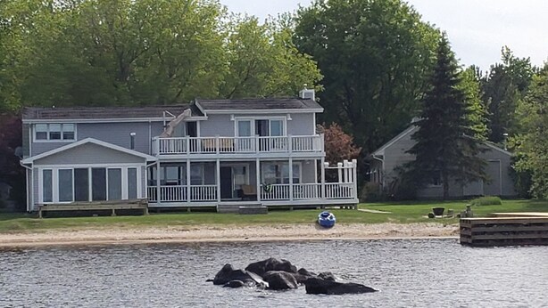 Una casa de dos pisos con balcón y un muelle que se adentra en el agua.