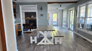Amplia sala de estar con piso de madera, una mesa central y una cocina al fondo.