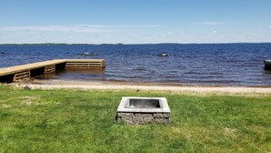 Un muelle de madera se extiende sobre un lago tranquilo, rodeado de zonas verdes y una estructura de piedra.