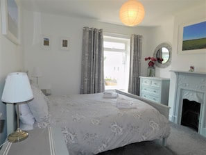 Une chambre à coucher avec un lit, une commode, un miroir, une lampe et une cheminée.