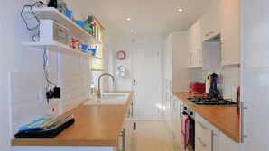 A modern kitchen with white cabinets, a wooden countertop, a sink, a stove, and a microwave. - Repton Cottage -  a cottage that sleeps 5 guests  in 2 bedrooms (Cromer)