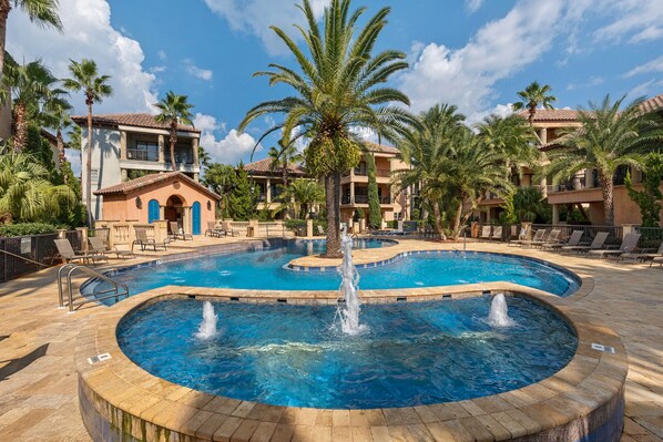 A pool area with a central fountain, surrounded by palm trees and lounge chairs.