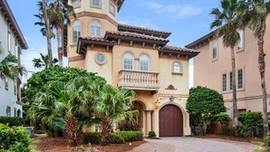 A Mediterranean-style building with a central courtyard, palm trees, and a brick pathway. - 🏖️ Beach Service Included! | 750 ft to Beach | 4 BR | Villa Tuscana (Miramar Beach)