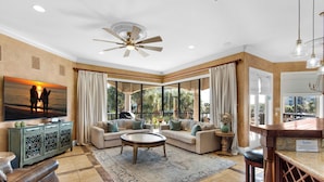 A spacious living room with a large window, a ceiling fan, and a television mounted on the wall. - 🏖️ Beach Service Included! | 750 ft to Beach | 4 BR | Villa Tuscana (Miramar Beach)