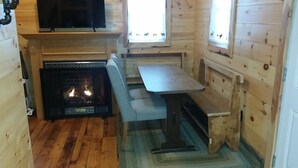 L’intérieur chaleureux d’un chalet avec une cheminée, un téléviseur fixé au-dessus et un banc près de la fenêtre.