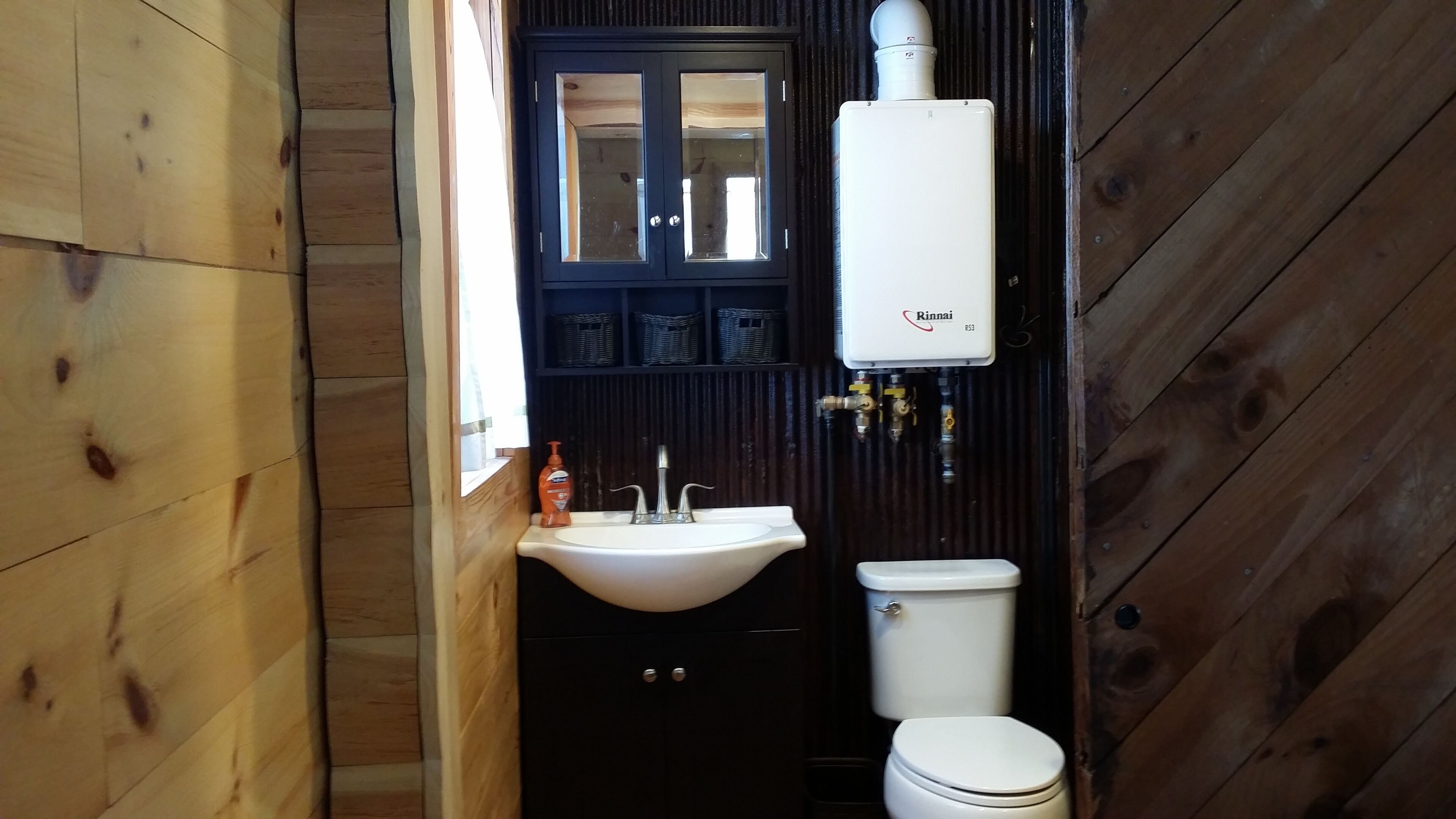 A compact bathroom with a white sink, a toilet, and a black cabinet. A white water heater is mounted above the sink.