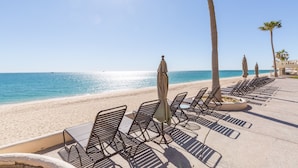 A beachside lounge with sun loungers and umbrellas, palm trees, and a clear view of the ocean. - Sonoran Sea West 407 Ocean View Condo (Puerto Peñasco)