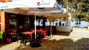 An outdoor seating area with red and green plastic chairs and tables, covered by umbrellas with Pepsi branding.