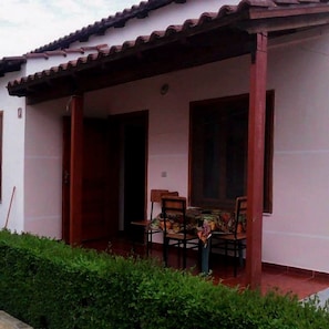 A building with a tiled roof, a covered porch with two wooden doors, and a small table with chairs.