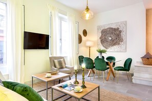 En moderne stue med sofa, sofabord, fjernsyn og et spiseområde med stole og bord.