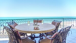 Una mesa redonda con seis sillas de mimbre, dos copas de vino y un plato de fresas en un balcón con vista al mar.