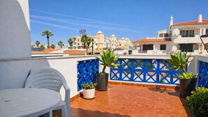 En terrasse med et hvidt bord og stole, plantekasser og et blåt hegn.