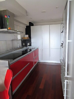 A modern kitchen with a red and white color scheme, stainless steel appliances, and a wooden floor. - Duplex San Luis - 1ªline beach, incredible view garage by Egona (Zarautz)