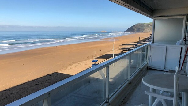 A balcony with a view of a sandy beach and ocean. There is a small table and two chairs. - Duplex San Luis - 1ªline beach, incredible view garage by Egona (Zarautz)