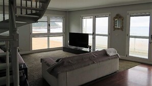 A spacious living room with a large TV, a sofa, and a staircase leading to a balcony overlooking the beach. - Duplex San Luis - 1ªline beach, incredible view garage by Egona (Zarautz)