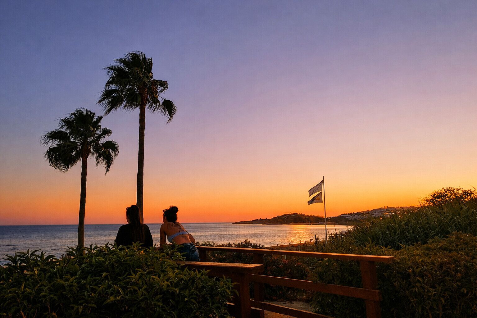 Sonnenuntergang mit Palmen und einer Flagge an einer Küstenpromenade.
