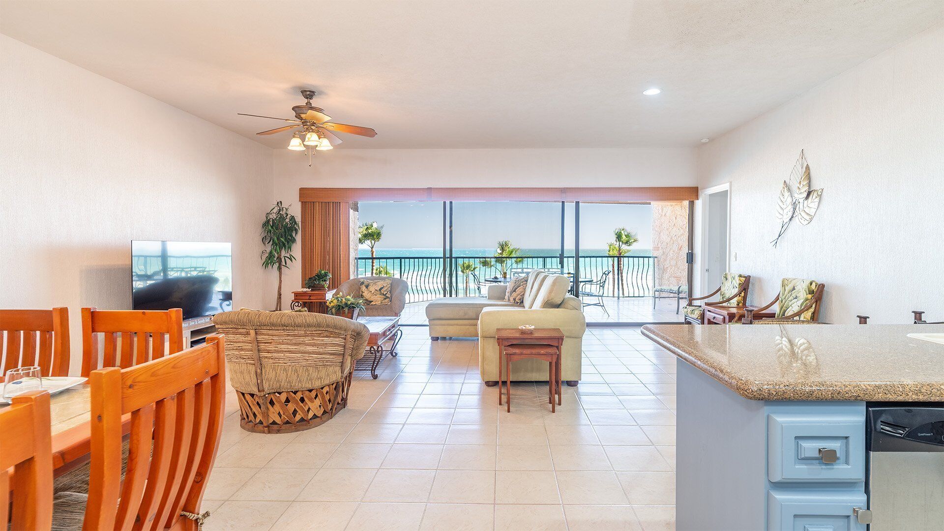 Amplia sala de estar con balcón con vistas al mar, comedor con mobiliario de madera y cocina con encimera de granito.
