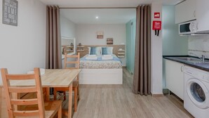Une chambre d’hôtel compacte comprenant une table à manger en bois, un lit avec une tête de lit, un lave-linge et un coin cuisine.