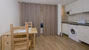 Une cuisine compacte équipée d’un lave-linge, d’un four à micro-ondes et d’un coin repas avec une table et des chaises.