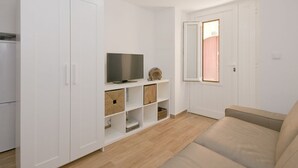 Un salon moderne avec un canapé beige, un téléviseur à écran plat posé sur un meuble blanc et des étagères intégrées avec des boîtes de rangement.