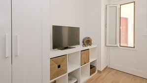 Une pièce avec un téléviseur posé sur une étagère blanche, un plancher en bois et une porte dotée d’un miroir.