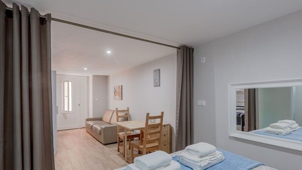 Une chambre d’hôtel moderne avec un lit, une petite table et un canapé. Il y a une fenêtre avec des rideaux, et des serviettes sont soigneusement pliées sur le lit.