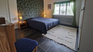 A bedroom with a bed, a nightstand, a chair, a patterned wall, a window with curtains, and a radiator. - House in Småland, ideal for children and dog owners with hiking trail at the house (Uppvidinge S)