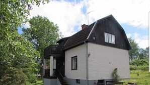 A two-story house with a gabled roof, a small porch, and a staircase leading to the entrance. - House in Småland, ideal for children and dog owners with hiking trail at the house (Uppvidinge S)